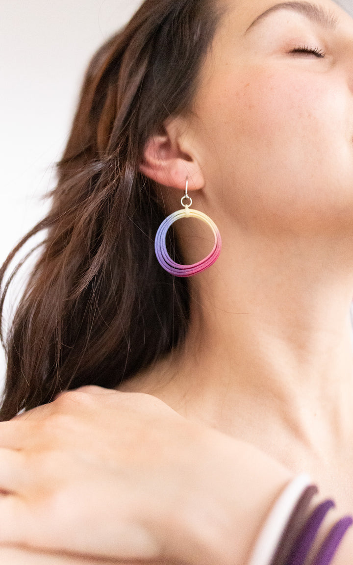 Jeune femme portant une boucle d’oreille ronde multicolore, inspirée d’un conte de fées. Bijou ultraléger en nylon recyclé, teinte artisanale éclatante. Design signé Vox & Oz, fait au Québec.
