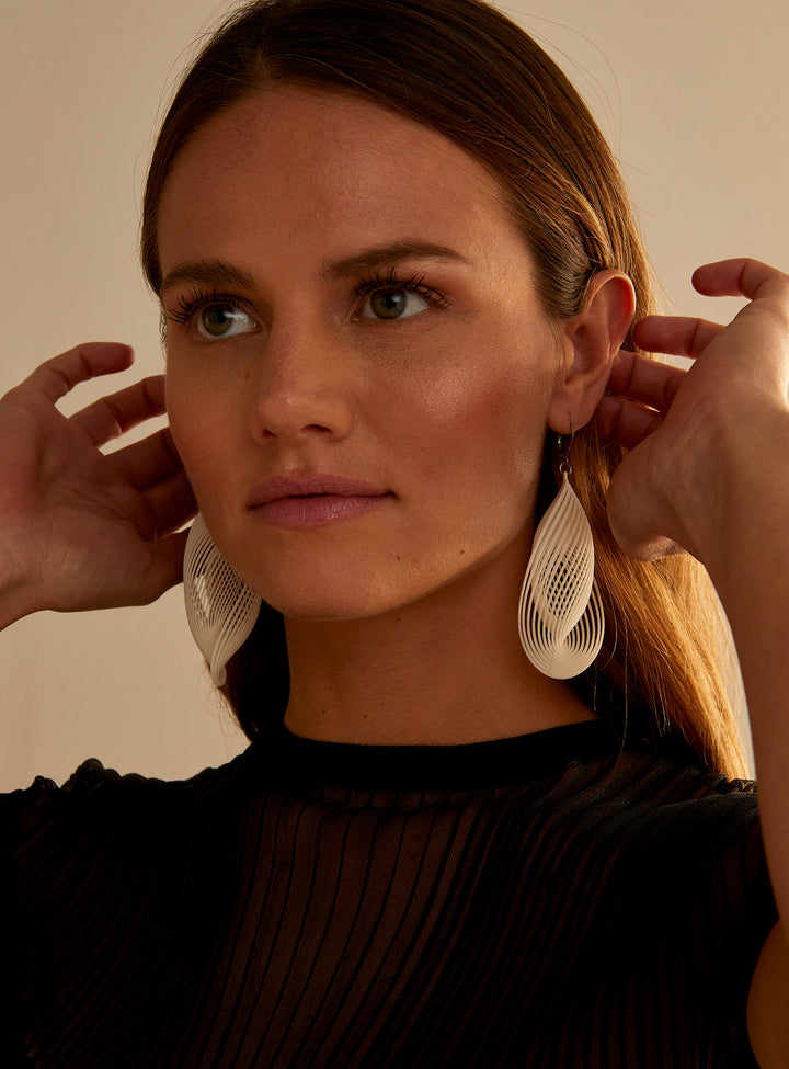 Portrait d’une femme portant les boucles d’oreilles OASIS ivoire ultralégères au design sculptural imprimé 3D signé Vox &amp; Oz