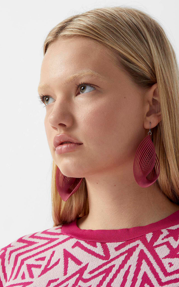 Portrait d’une femme portant les boucles d’oreilles OASIS fuchsia ultralégères au design sculptural imprimé 3D signé Vox &amp; Oz