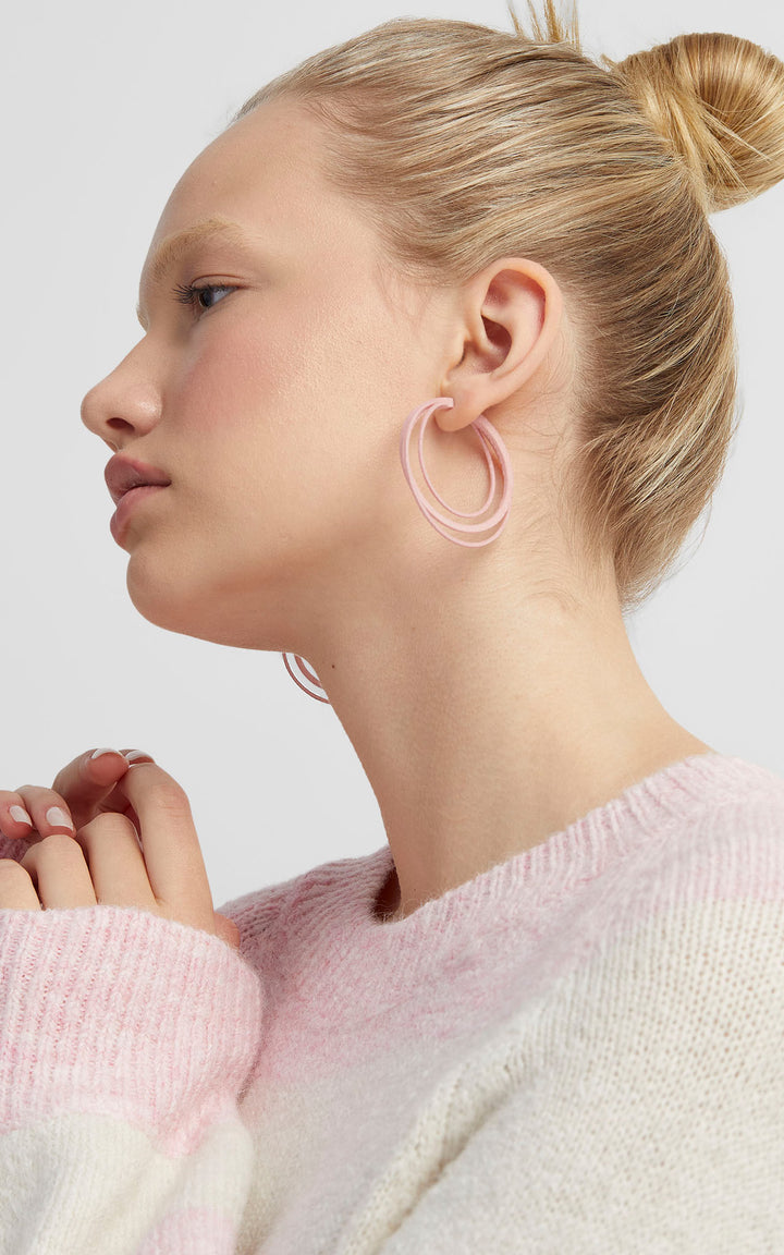 Les anneaux triple cerceaux entrelacés Daily de Vox & Oz. Couleur rose. portér par une jenne fille au cheveux blond attaché en chignon.