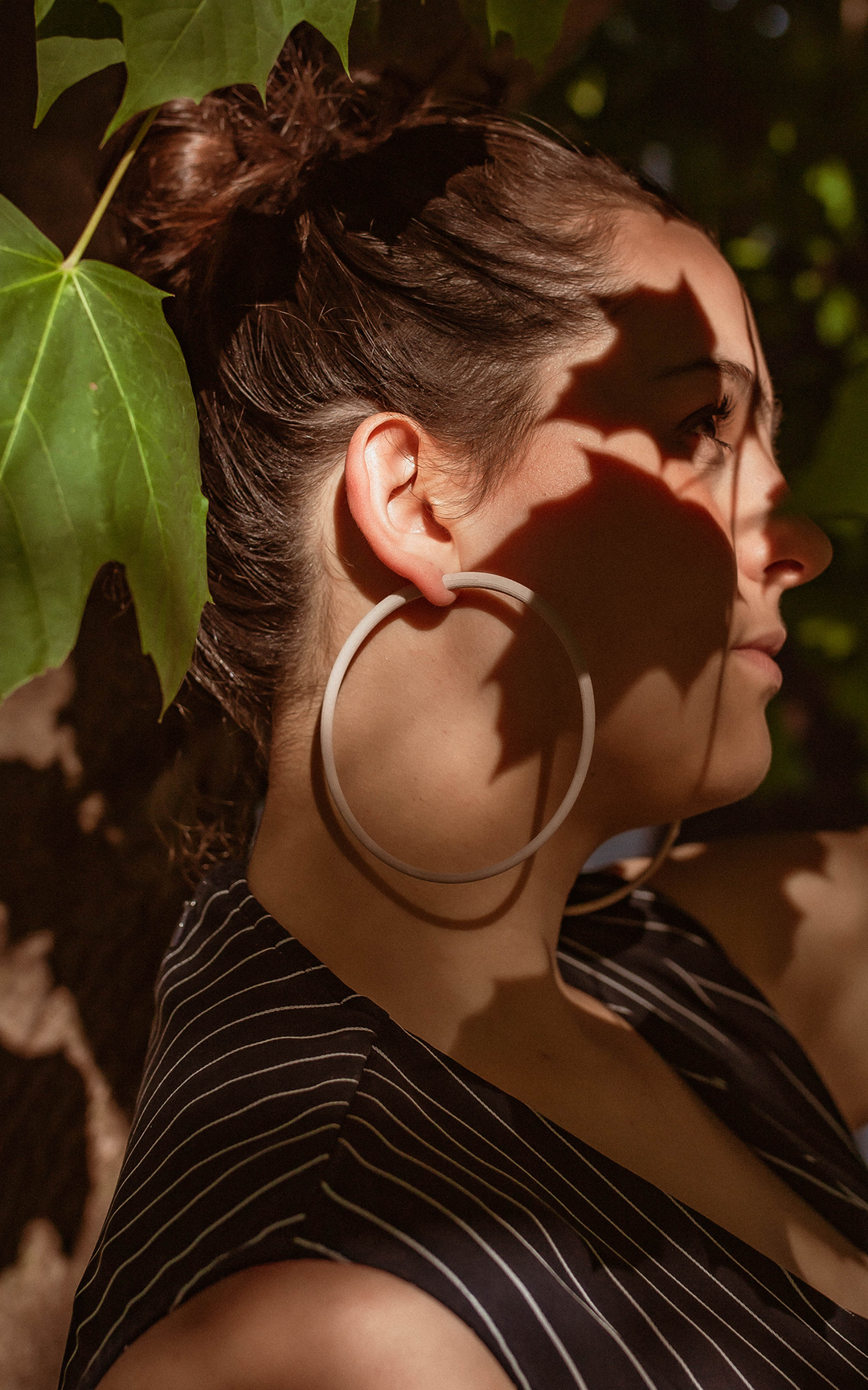 Les anneaux Atlas 10 cm De grands anneaux ultralégers ! Un poids plume !   Confort et design aux lignes minimalistes au tracé épais. Porter part jheun femme chignon cheveux bruns.  Saison automne. Ombrage d'une feuille d'érable.  Couleur ivoir blanc os.