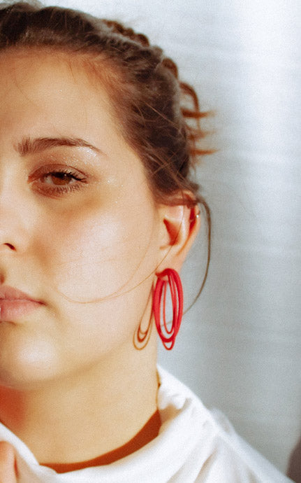Les anneaux triple cerceaux entrelacés Daily de Vox & Oz. Couleur rouge. Porter à l'oreille par une jeune femme cheveux bruns, chemisier blanc.