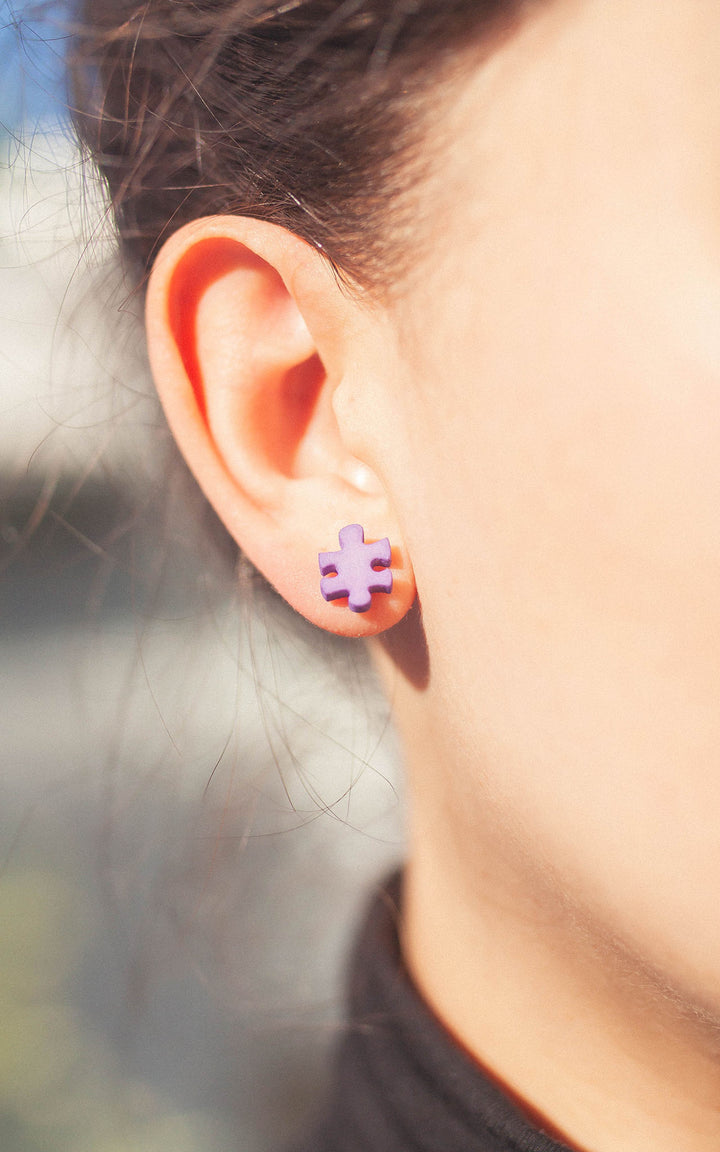 Femme qui porte un bijou en forme de casse-tete à son lobe d'oreille. Casse-tete mauve. 